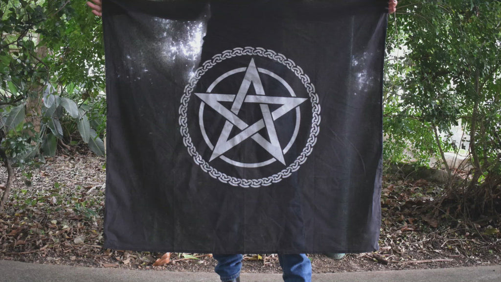Person waving a large black cotton altar cloth, witches flag tapestry with a tree of life celtic knot circling a white pentagram pentacle