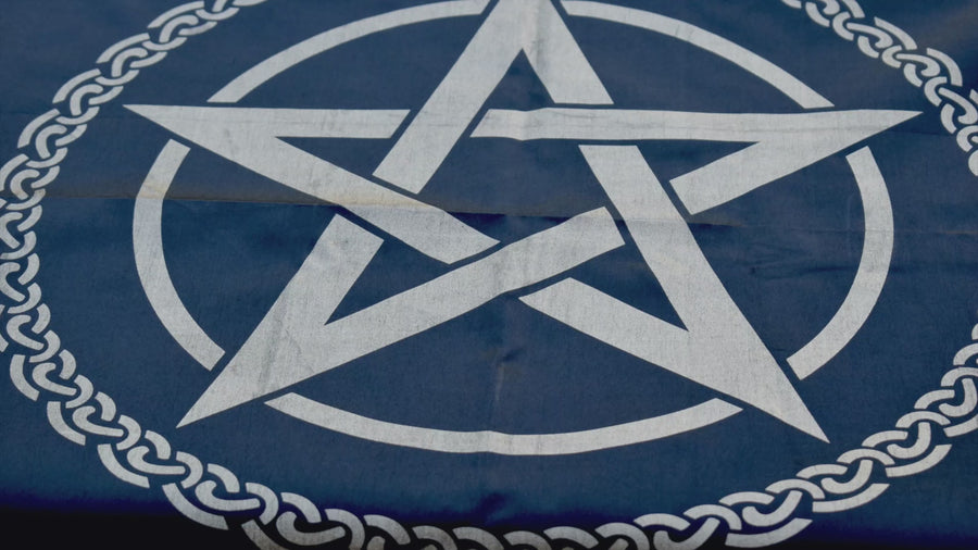 A black satin altar cloth or witches flag with gold pentagram pentacle in the middle encircled by a celtic knot resting on autumn leaves