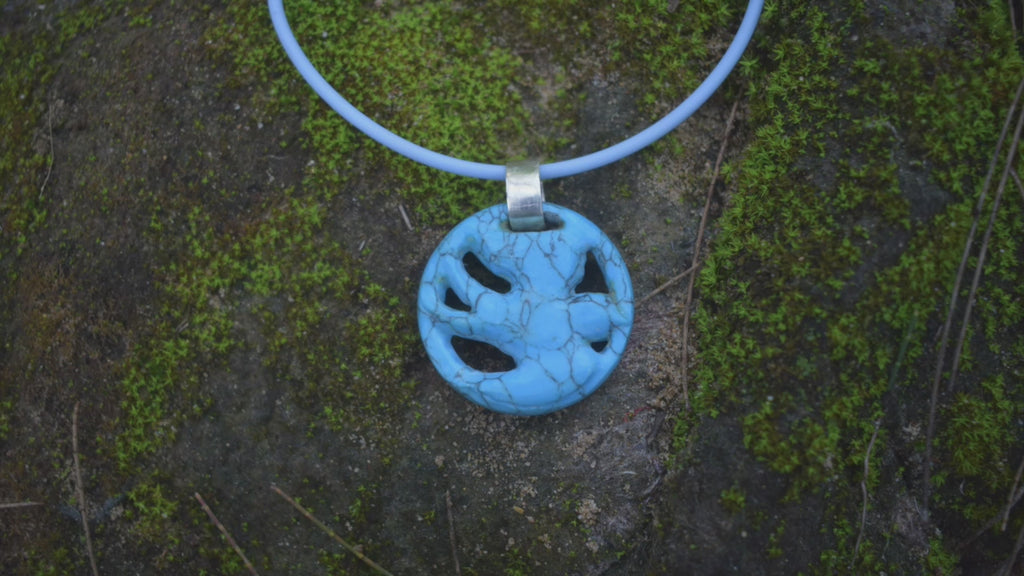A pendant carved into the shape of a flying bird made from blue howlite crystal sits around a person's neck