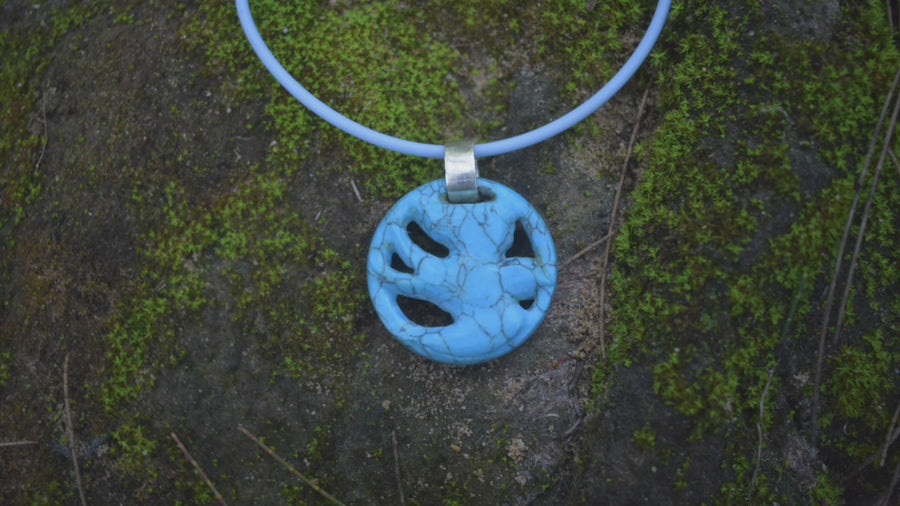 A pendant carved into the shape of a flying bird made from blue howlite crystal sits around a person's neck