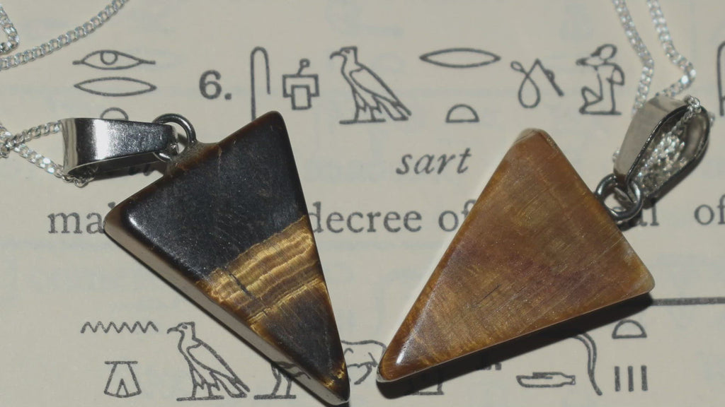 Three tiger's eye triangle pendants on silver chains resting on egyptian hieroglyphic parchment
