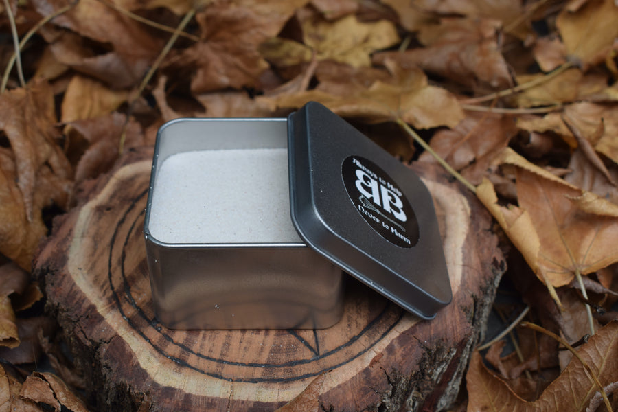 A tin of white sand resting on a wooden pentagram trivet nestled in a bed of autumn leaves