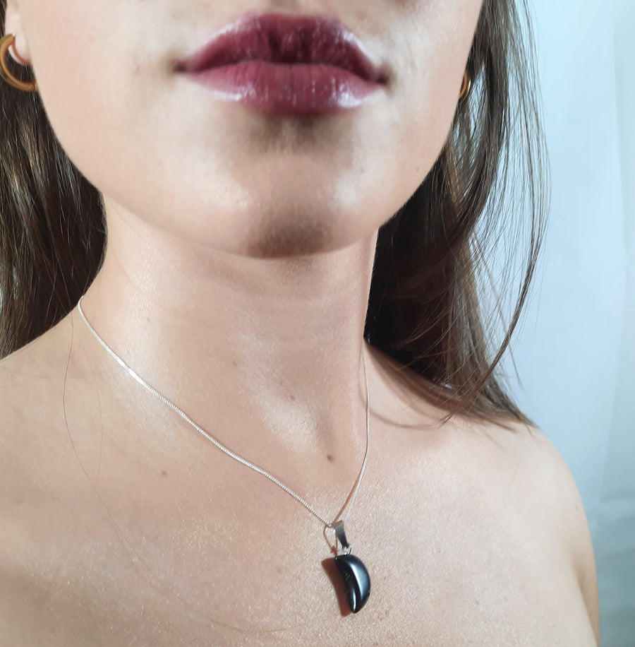 A black tourmaline crystal crescent moon necklace on a sterling silver chain hanging on the neck of a person