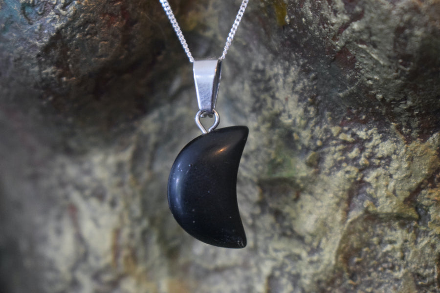 A black tourmaline crystal crescent moon necklace on a sterling silver chain hanging on the neck of a bronze sculpture