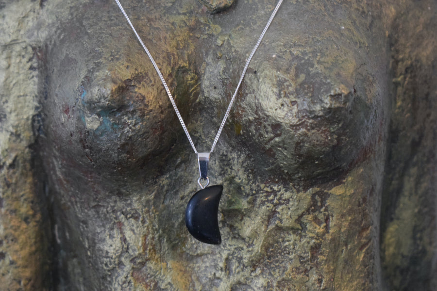 A black tourmaline crystal crescent moon necklace on a sterling silver chain hanging on the neck of a bronze goddess sculpture