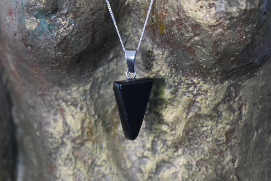 A black tourmaline crystal inverted triangle necklace on a sterling silver chain hanging on the neck of a bronze goddess sculpture