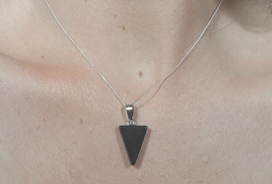 A black tourmaline crystal inverted triangle necklace on a sterling silver chain hanging on the neck of a person