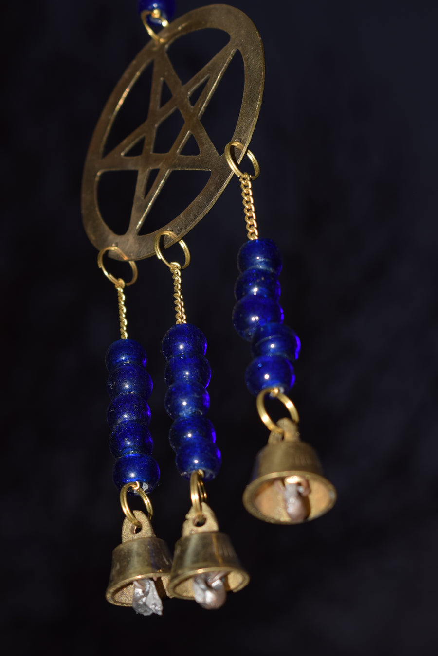 A bronze pentagram metal wind chime with royal blue beads and bells hanging in the garden in the breeze