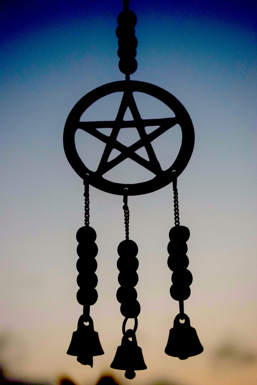 A pentagram bronze metal wind chime with beads and bells hanging in the garden silhouetted against the sky