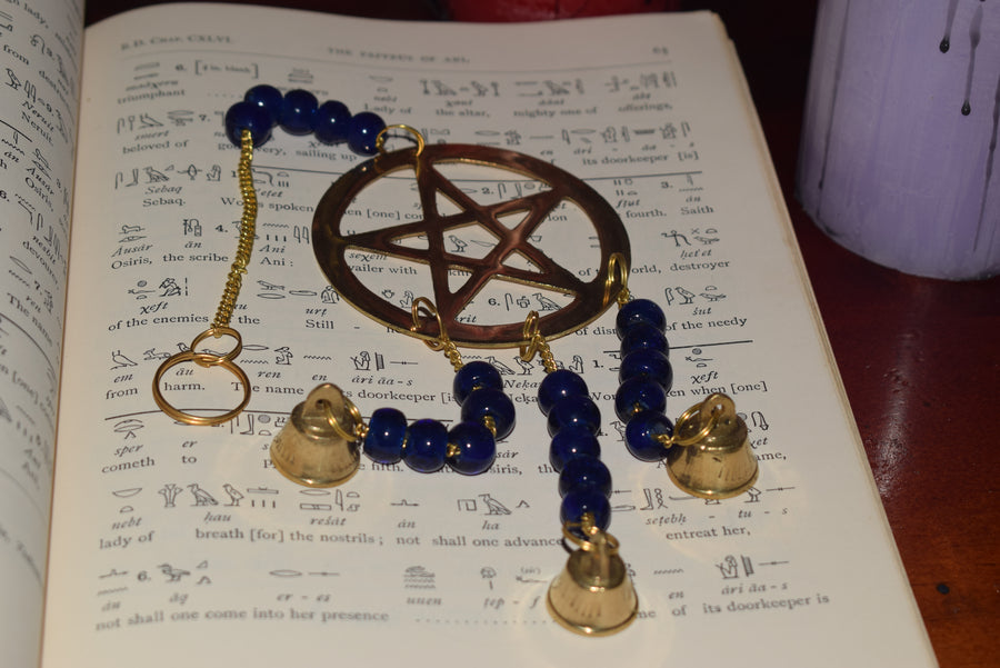 A bronze pentagram metal wind chime with royal blue beads and bells resting on a page of hieroglyphics