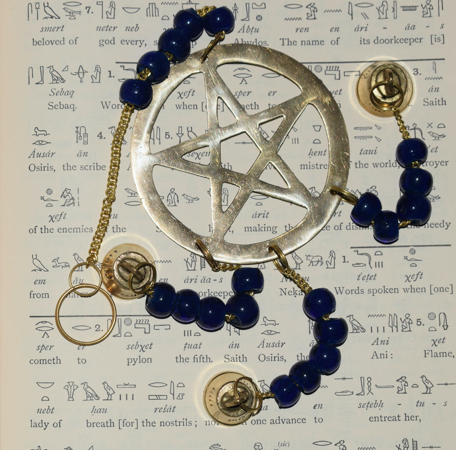A bronze pentagram metal wind chime with royal blue glass beads and bells resting on a page of hieroglyphics