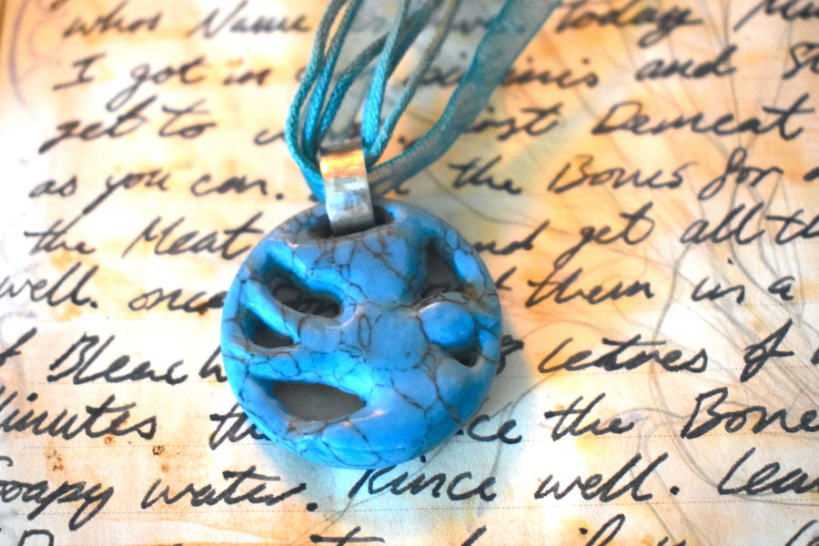 A pendant carved into the shape of a flying bird made from blue howlite crystal sits on a page of handwriting