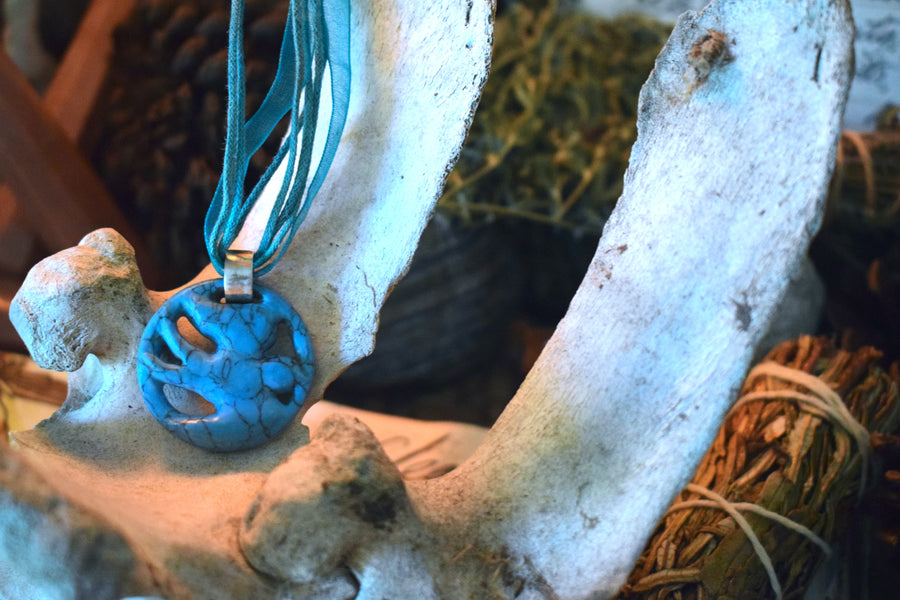 A pendant carved into the shape of a flying bird made from blue howlite crystal sits on an old cow bone