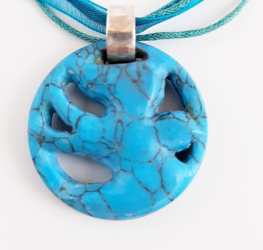A pendant carved into the shape of a flying bird made from blue howlite crystal sits on a white background