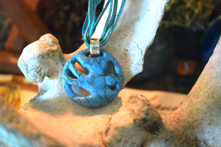 A pendant carved into the shape of a flying bird made from blue howlite crystal sits on a cow bone