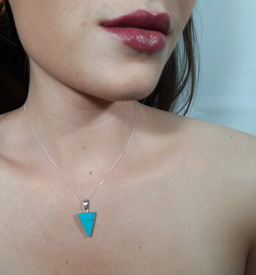 A blue howlite crystal inverted triangle necklace on a sterling silver chain hanging on the neck of a person
