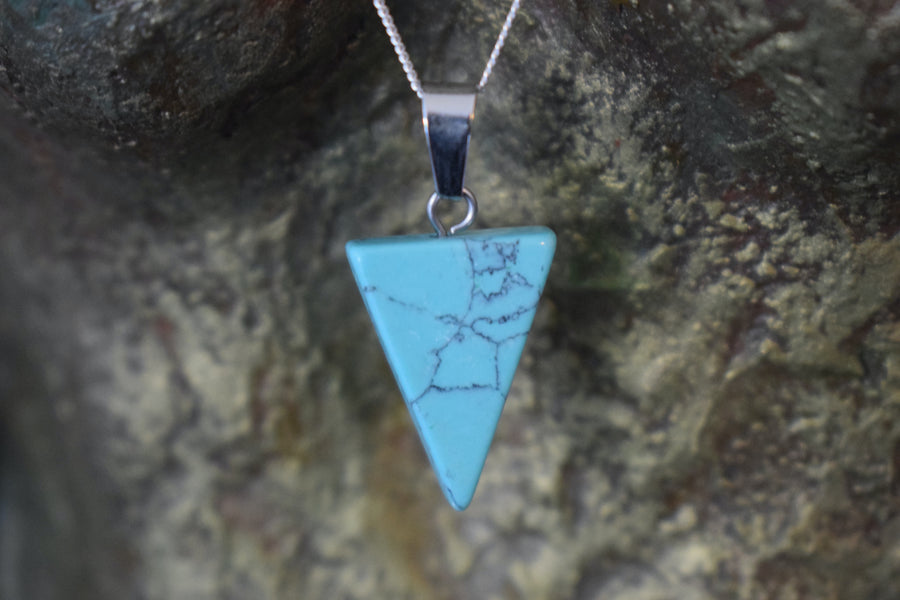 A blue howlite crystal inverted triangle necklace on a sterling silver chain hanging on the neck of a bronze sculpture