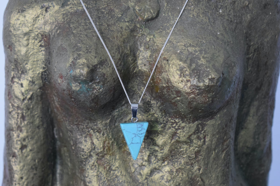 A blue howlite crystal inverted triangle necklace on a sterling silver chain hanging on the neck of a bronze goddess sculpture
