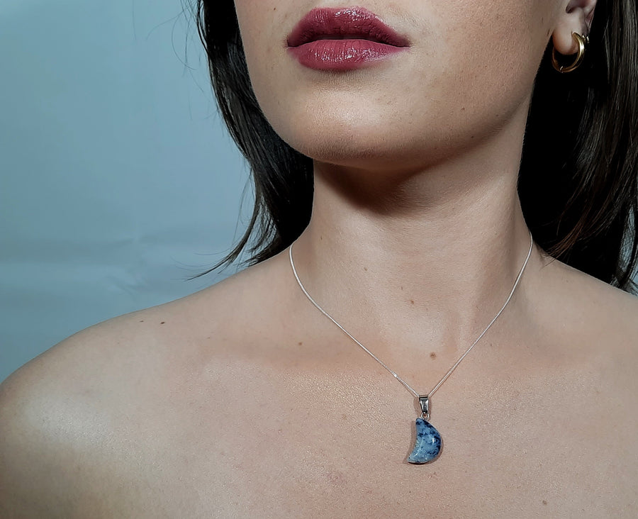 A sodalite crystal crescent moon necklace on a sterling silver chain hanging on the neck of a person