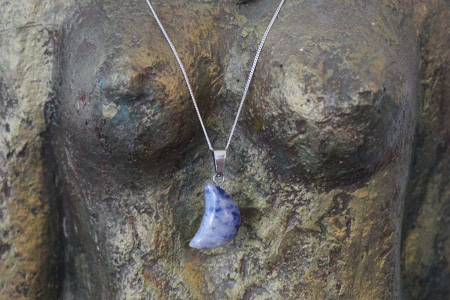 A sodalite crystal crescent moon necklace on a sterling silver chain hanging on the neck of a bronze goddess sculpture