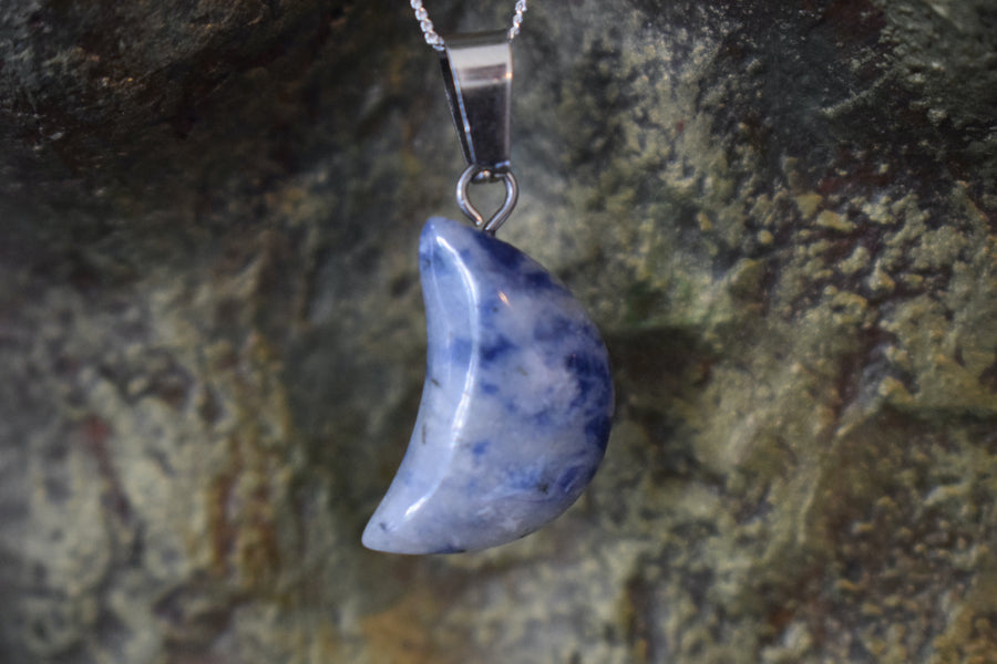 A sodalite crystal crescent moon necklace on a sterling silver chain with a bronze sculpture background