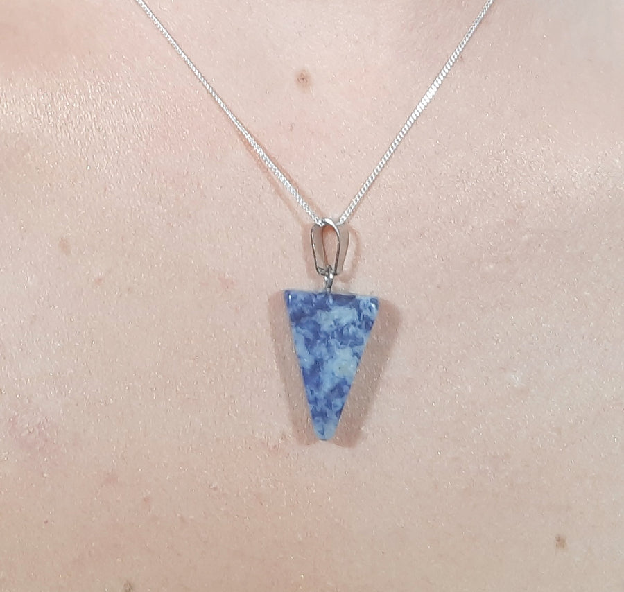 A blue sodalite crystal inverted triangle necklace on a sterling silver chain hanging on the neck of a person
