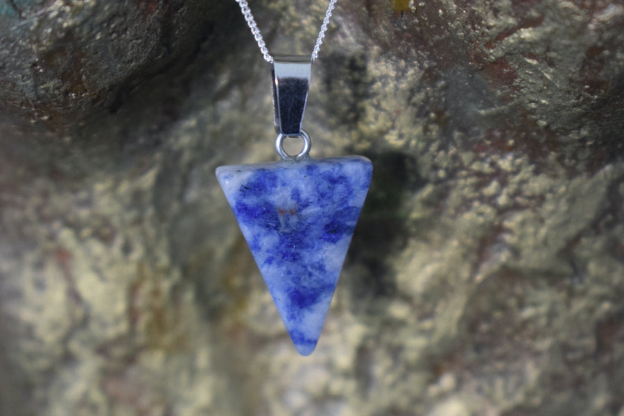 A blue sodalite crystal inverted triangle necklace on a sterling silver chain hanging on the neck of a bronze sculpture