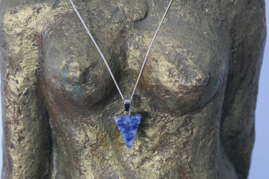 A blue sodalite crystal inverted triangle necklace on a sterling silver chain hanging on the neck of a bronze goddess sculpture