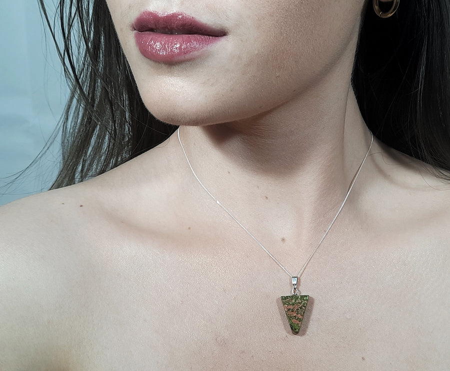 A unakite crystal inverted triangle necklace on a sterling silver chain hanging on the neck of a person