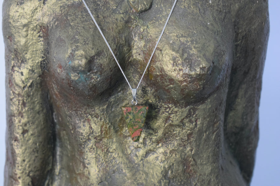 A unakite crystal inverted triangle necklace on a sterling silver chain hanging on the neck of a bronze goddess sculpture