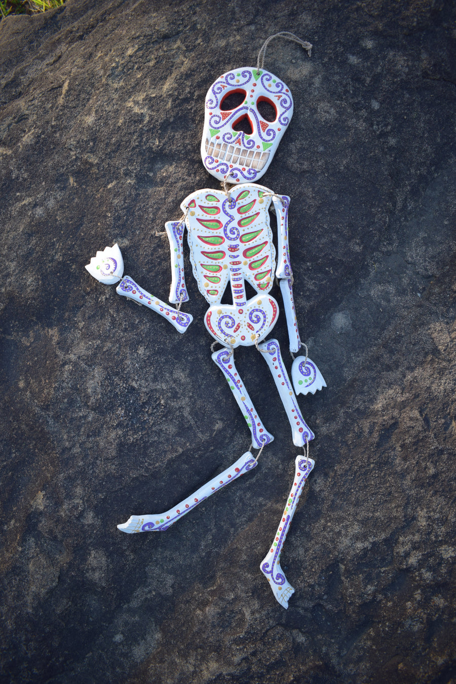 A colourful calaca Day of the Dead spirit medicine rattle resting on a rock