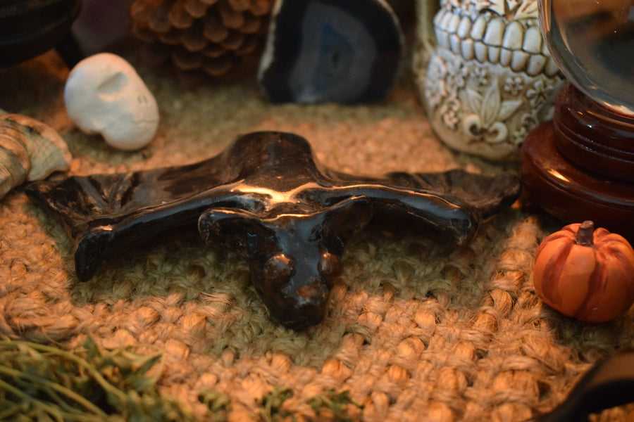 A handmade ceramic flying fox bat resting on an altar with herbs and crystals in the background