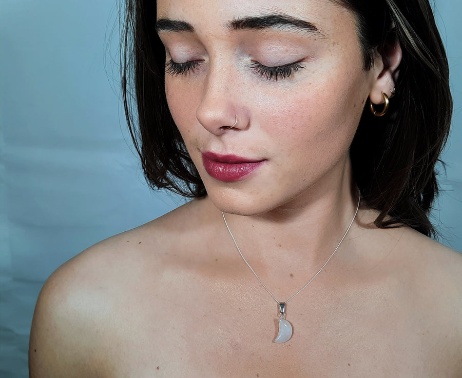 A clear quartz crystal crescent moon necklace on a sterling silver chain hanging on the neck of a person