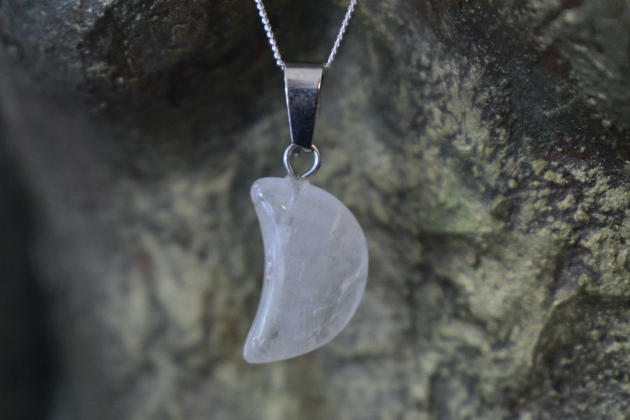 A clear quartz crystal crescent moon necklace on a sterling silver chain hanging on the neck of a bronze sculpture