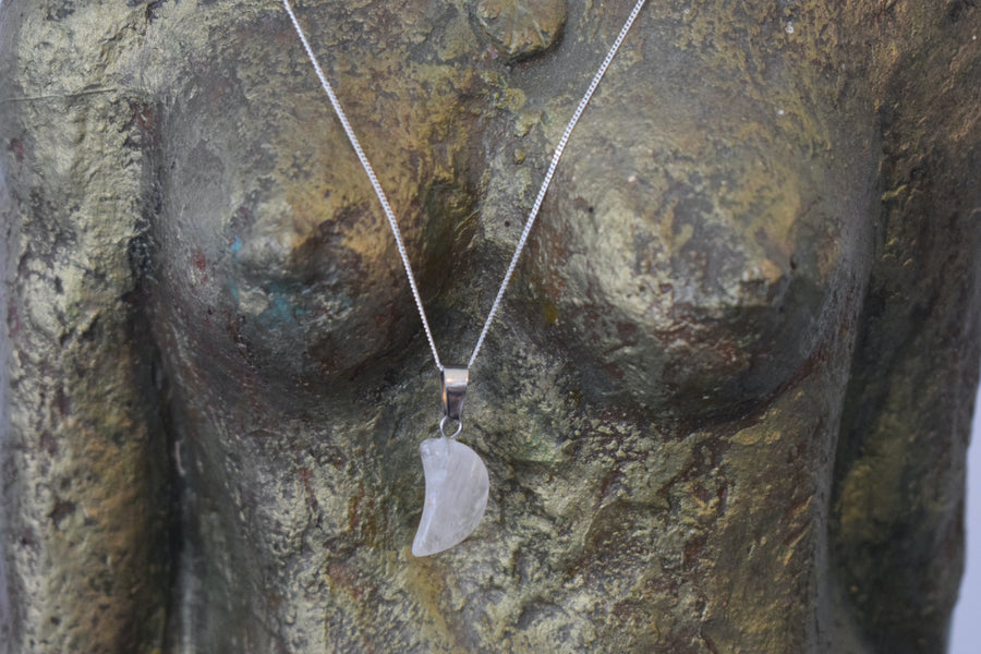 A clear quartz crystal crescent moon necklace on a sterling silver chain hanging on the neck of a bronze goddess sculpture