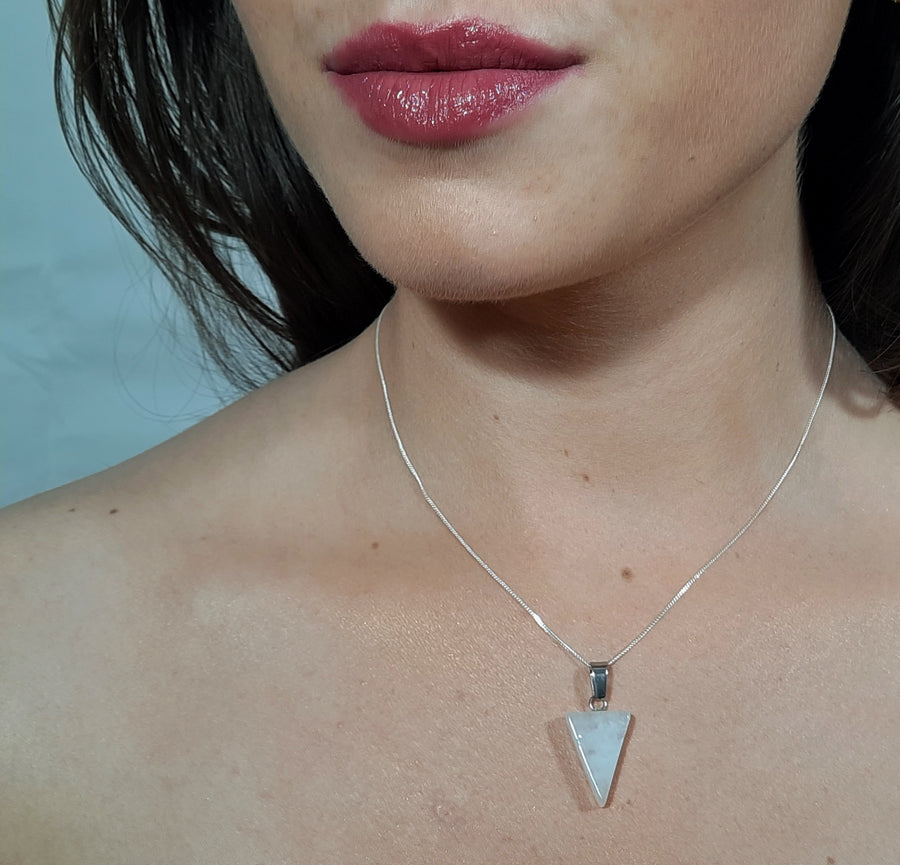 A clear quartz crystal inverted triangle necklace on a sterling silver chain hanging on the neck of a person