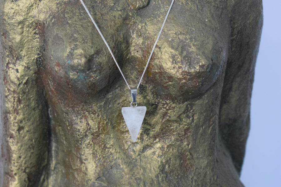 A clear quartz crystal inverted triangle necklace on a sterling silver chain hanging on the neck of a bronze goddess sculpture