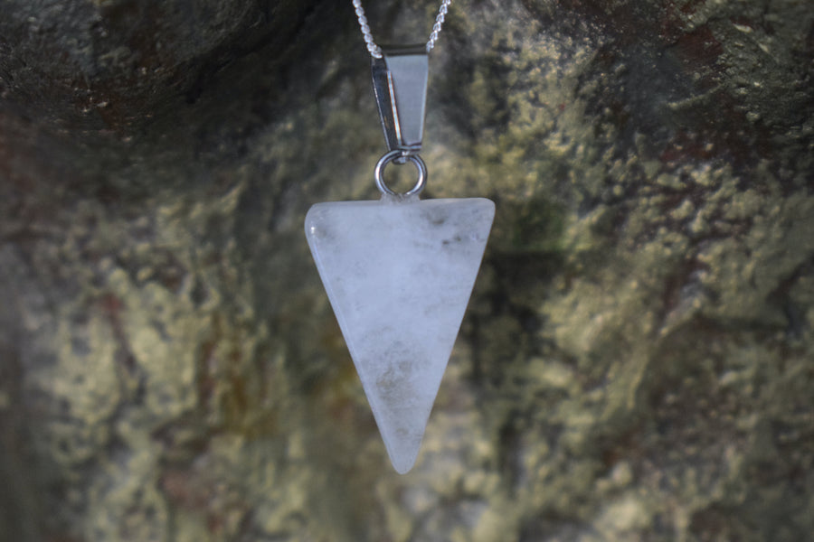 A clear quartz crystal inverted triangle necklace on a sterling silver chain hanging on the neck of a bronze sculpture