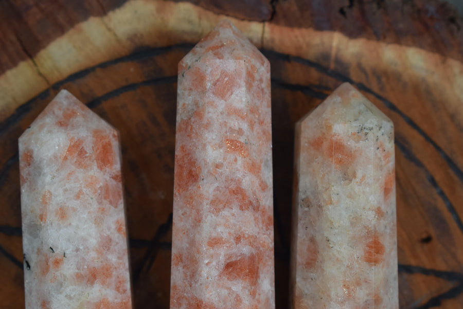 3 sunstone, heliolite or aventurescent crystal wands, points, towers or obelisks resting on timber disk with pentagram pentacle wood burning