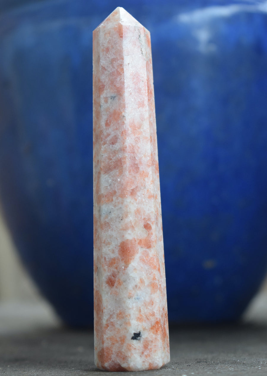 Sunstone, heliolite or aventurescent crystal wand, point, tower or obelisk with blue planter box in background