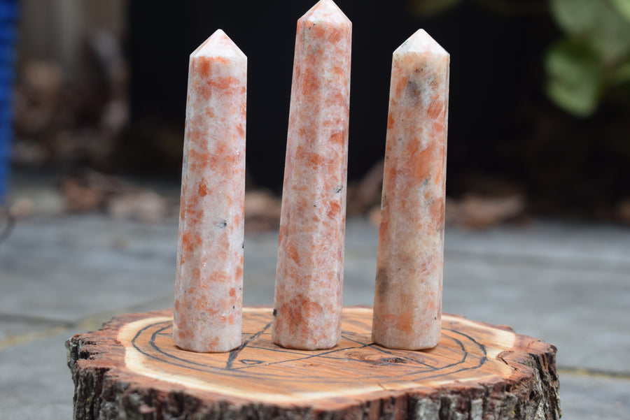 Three sunstone, heliolite or aventurescent crystal wands, points, towers or obelisks sitting on timber disk with pentagram pentacle pyrogravure
