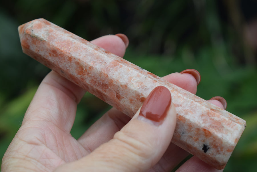 Hand holding a sunstone, heliolite or aventurescent crystal wand, point, tower or obelisk 