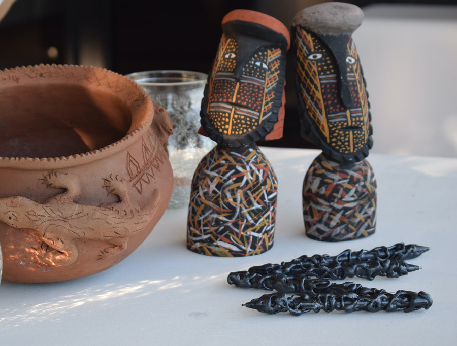 Four black handcrafted pens on a table with primitive sculptures and ceramic bowl