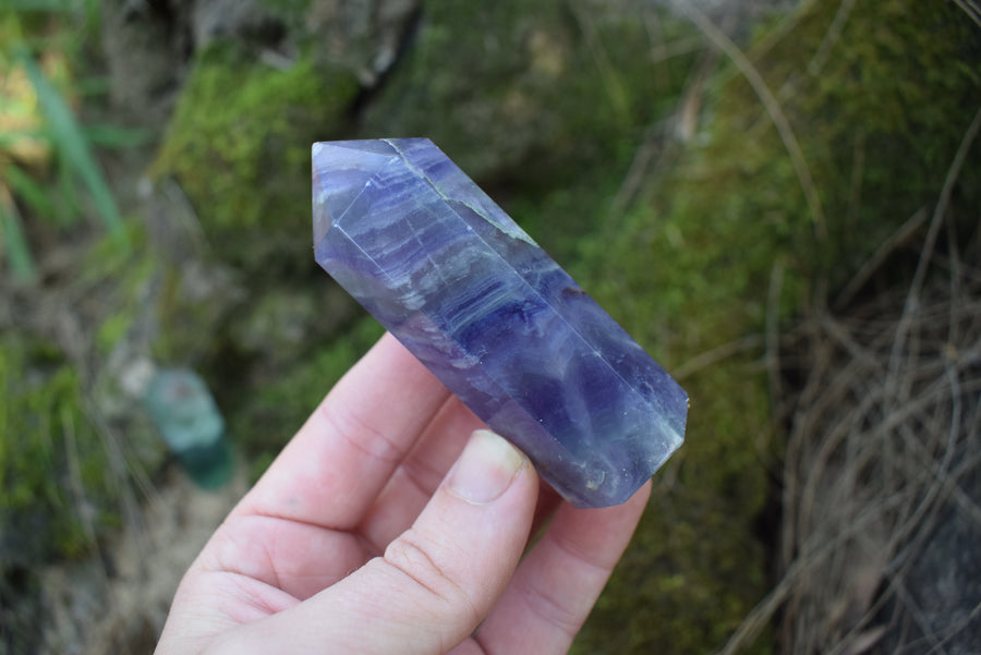 A purple fluorite crystal point being held by a hand