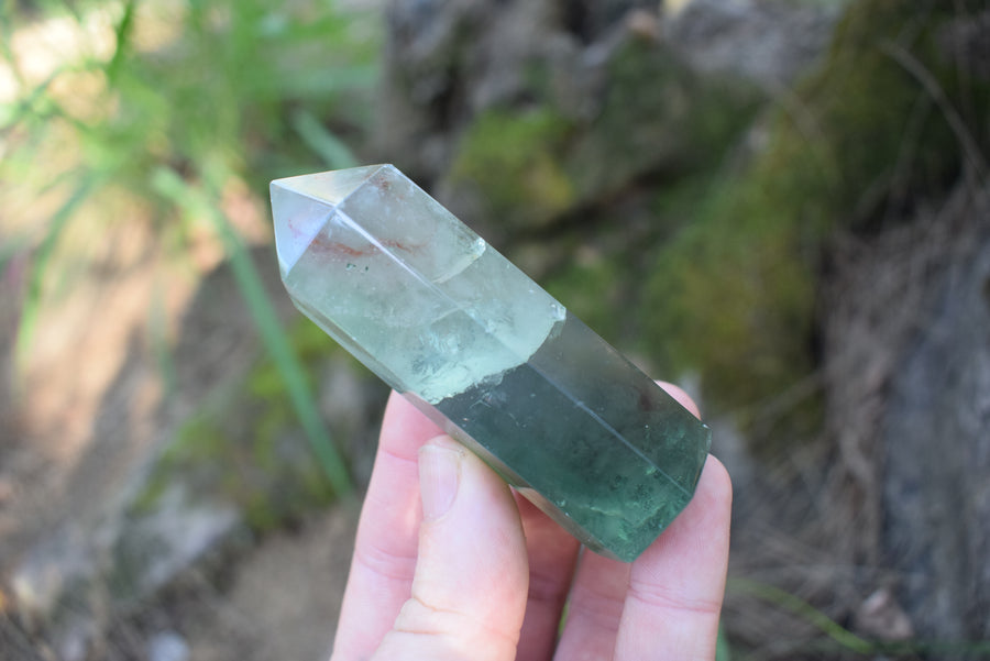 A hand holding a green fluorite crystal point 