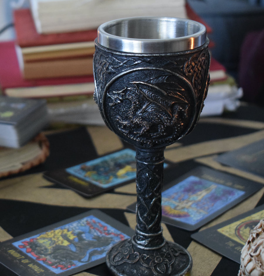 A goblet with a 3d black dragon rests on an altar with tarot cards and books