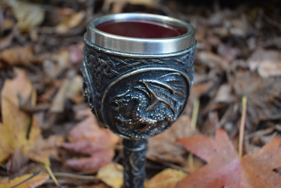 A goblet with a 3d black dragon rests filled with red wine on a bed of autumn leaves