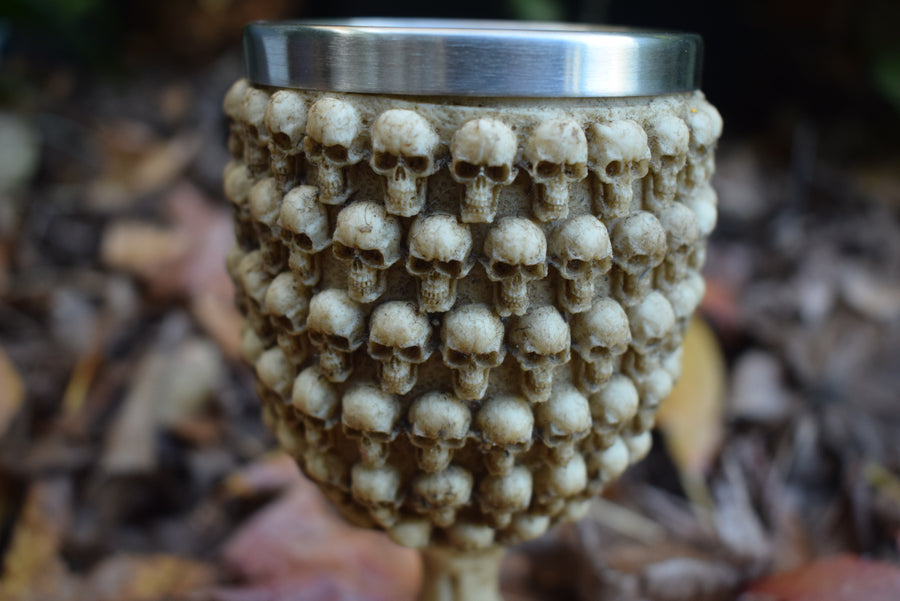 A goblet with skulls all over it sits on a bed of autumn leaves