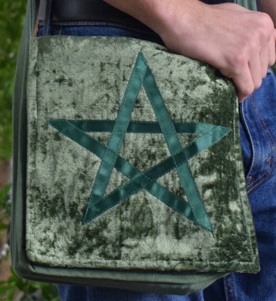 Hand resting on green velvet shoulder bag with pentagram on the front