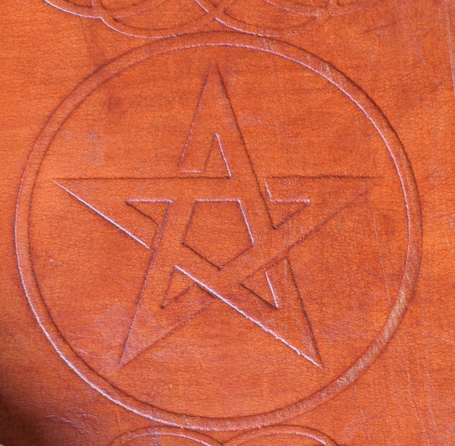 A leather-bound book of shadows with a pentagram pentacle and celtic knots embossed on the cover 